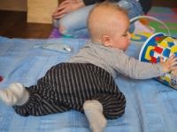 Ein Baby liegt auf dem Bauch und spielt mit einer runden Bauklotz-Box.