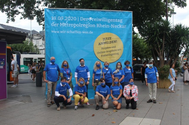 Gruppenfoto vor dem blauen Würfel, der am Heidelberger Bismarckplatz auf den Freiwilligentag hinweist. 