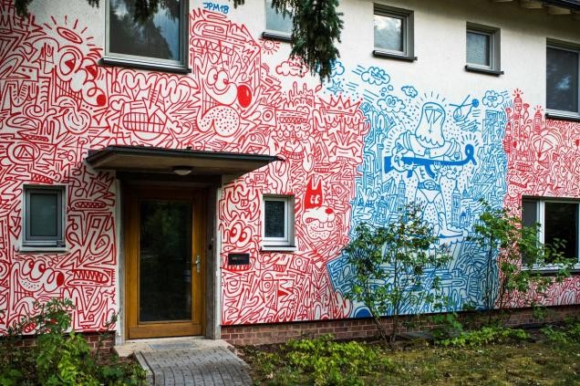 Eine Hauswand wurde um die Eingangstür herum mit roten und blauen Linienmustern bemalt. In den Linien erkennt man Comicfiguren und Gesichter. (Foto: IBA/Dittmer)