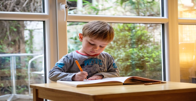 Ein Kind sitzt an einem Tisch und malt mit einem Stift in ein Heft.