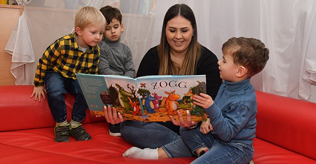 Drei Kinder beim Vorlesen mit einer Erzieherin