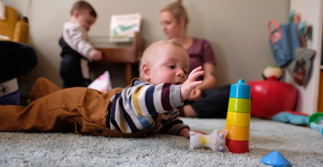 Ein Baby liegt auf einem Teppich mit Spielsachen und greift nach Bauklötzen. 