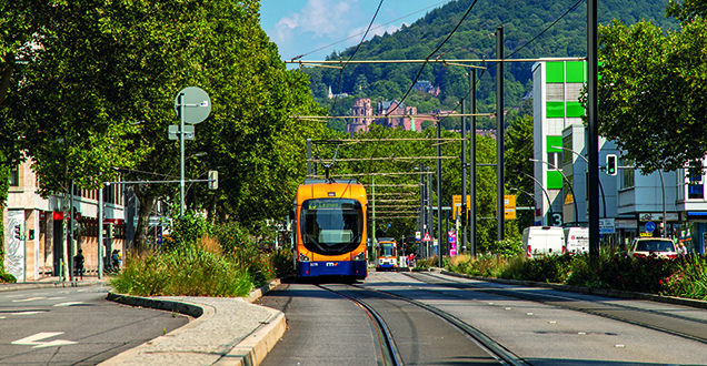 Man sieht eine orangefarbene Straßenbahn in Heidelberg, im Hintergrund ist das Heidelberger Schloss.