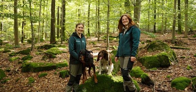 Zwei Frauen in Funktionskleidung mit zwei Hunden im Wald