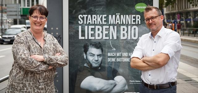 Hafner und Schmidt-Lamontain vor Plakat mit Aufschrift starke Männer lieben Bio und Mann, der die Arme verschränkt hat