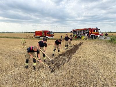 Durch das Anlegen eines sogenannten Wundstreifens – auch Feuerschneise genannt – wird verhindert, dass sich das Feuer weiter ausbreitet. (Foto: Feuerwehr Heidelberg) Feuerwehrleute mit Harken auf einem Feld