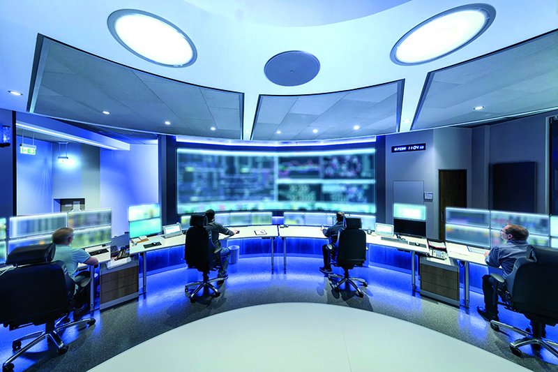 Vier Mitarbeiter sitzen vor mehreren Monitoren