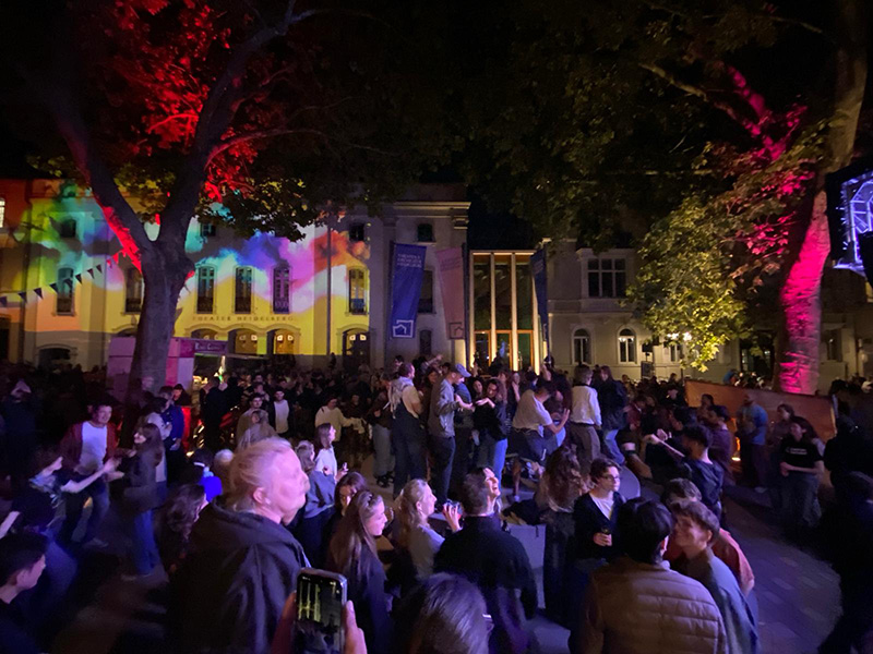 Menschen auf dem Theaterplatz, das Theater ist bunt angeleuchtet