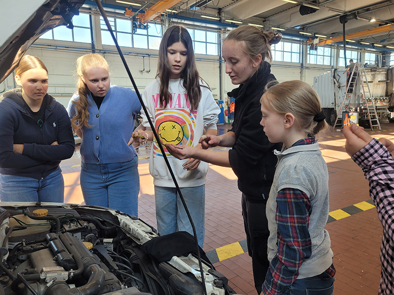 Fünf Mädchen mit Kfz-Mechanikerin vor offener Motorhaube