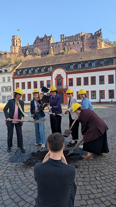 Sechs Frauen mit Bauhelmen auf dem Kopf simulieren einen Spatenstich