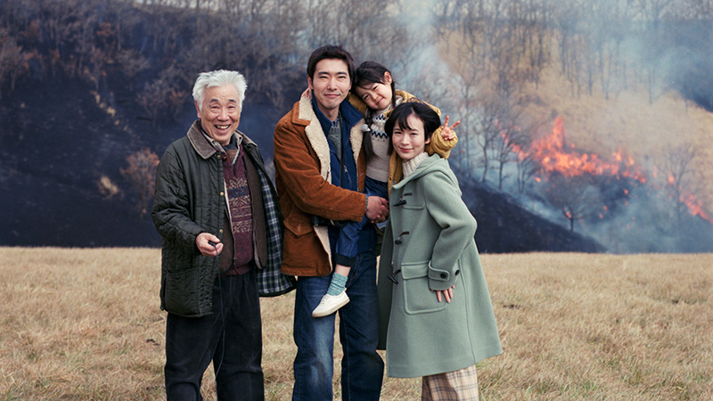 Japanische Familie mit Großvater, Eltern und kleiner Tochter posiert vor Waldbrand