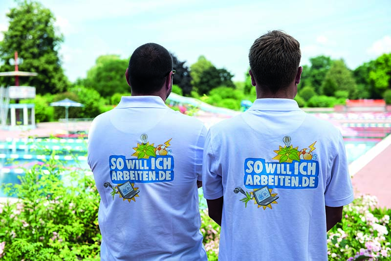 Zwei Männer von hinten mit weißen Polohemden und der Aufschrift "So will ich arbeiten"